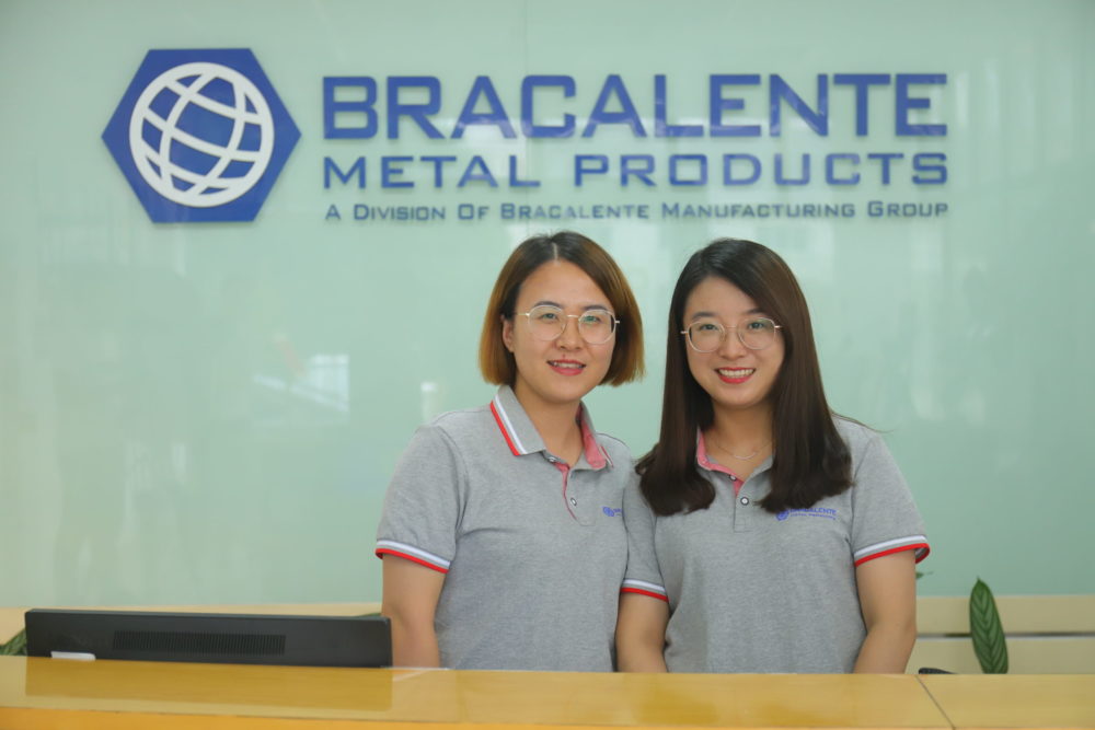 two female bracalente team members smiling behind a bracalente desk